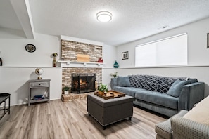 A living room with a fireplace, a grey sofa, a small table, and a wooden floor.