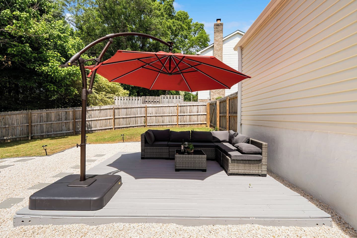 Een terras buiten met een modulaire bank, een rode parasol en een houten terras.