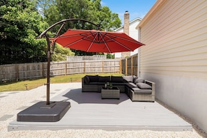 An outdoor patio with a sectional sofa, a red umbrella, and a wooden deck.