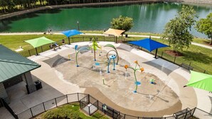 A water play area with a circular design, surrounded by a fence, and a body of water in the background. - Near Carowinds ~ 4BR w/ Game Room & Splash Pad (Pineville)