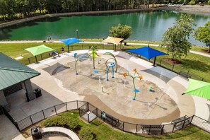 A water play area with a circular design, surrounded by a fence, near a body of water and trees.