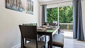 A dining area with a table set for four, chairs, a painting on the wall, and a view of a deck and greenery outside. - Near Carowinds ~ 4BR w/ Game Room & Splash Pad (Pineville)