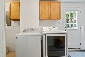 A laundry room with a front-loading washer and dryer, wooden cabinets above, and a door with a window to the outside.