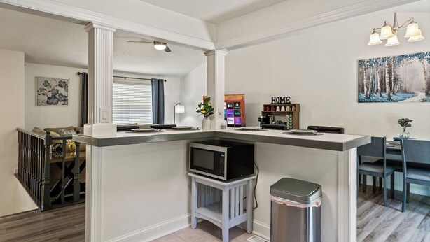 A modern kitchen with a built-in microwave, a trash can, and a dining area with a table and chairs. - Near Carowinds ~ 4BR w/ Game Room & Splash Pad (Pineville)