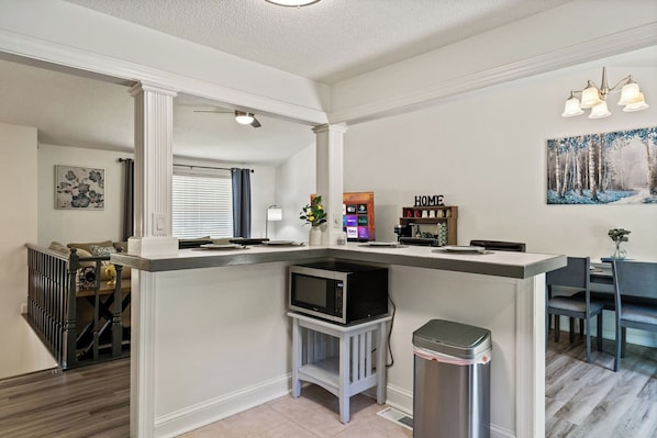 A modern kitchen with a built-in microwave, a trash can, and a dining area with a table and chairs.