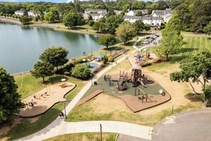 A park with playground equipment, a walking path, and a lake.