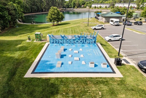 A swimming pool with a blue deck, surrounded by grass and a parking area with vehicles.