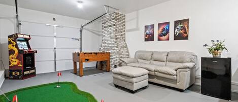 A room with a foosball table, a sofa, a small table with a plant, and a wall with three framed artworks.