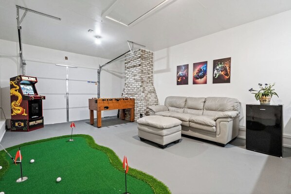 A room with a foosball table, a sofa, a small table with a plant, and a wall with three framed artworks.