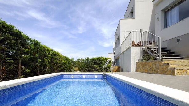Une piscine à l’eau d’un bleu cristallin, entourée d’un bâtiment moderne à la façade en pierre et dotée d’un escalier menant à un niveau supérieur.