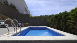 Une piscine rectangulaire avec un escalier en métal, entourée d’une terrasse en bois et d’un bâtiment blanc.