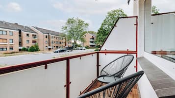 A balcony with a view of a residential street, featuring a wooden floor and two black wicker chairs.