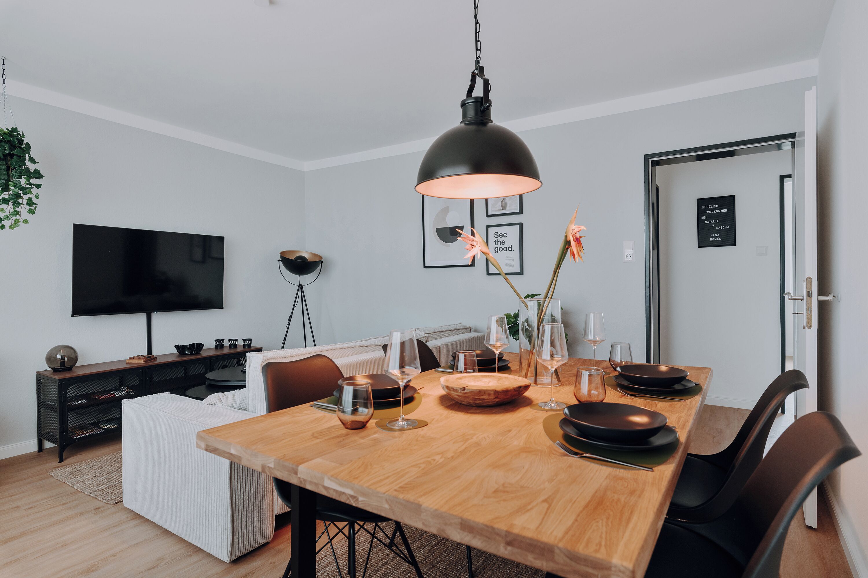 A modern dining area with a wooden table, black chairs, and a hanging pendant light.