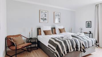 A modern bedroom with a large bed, a leather armchair, and two framed pictures on the wall.