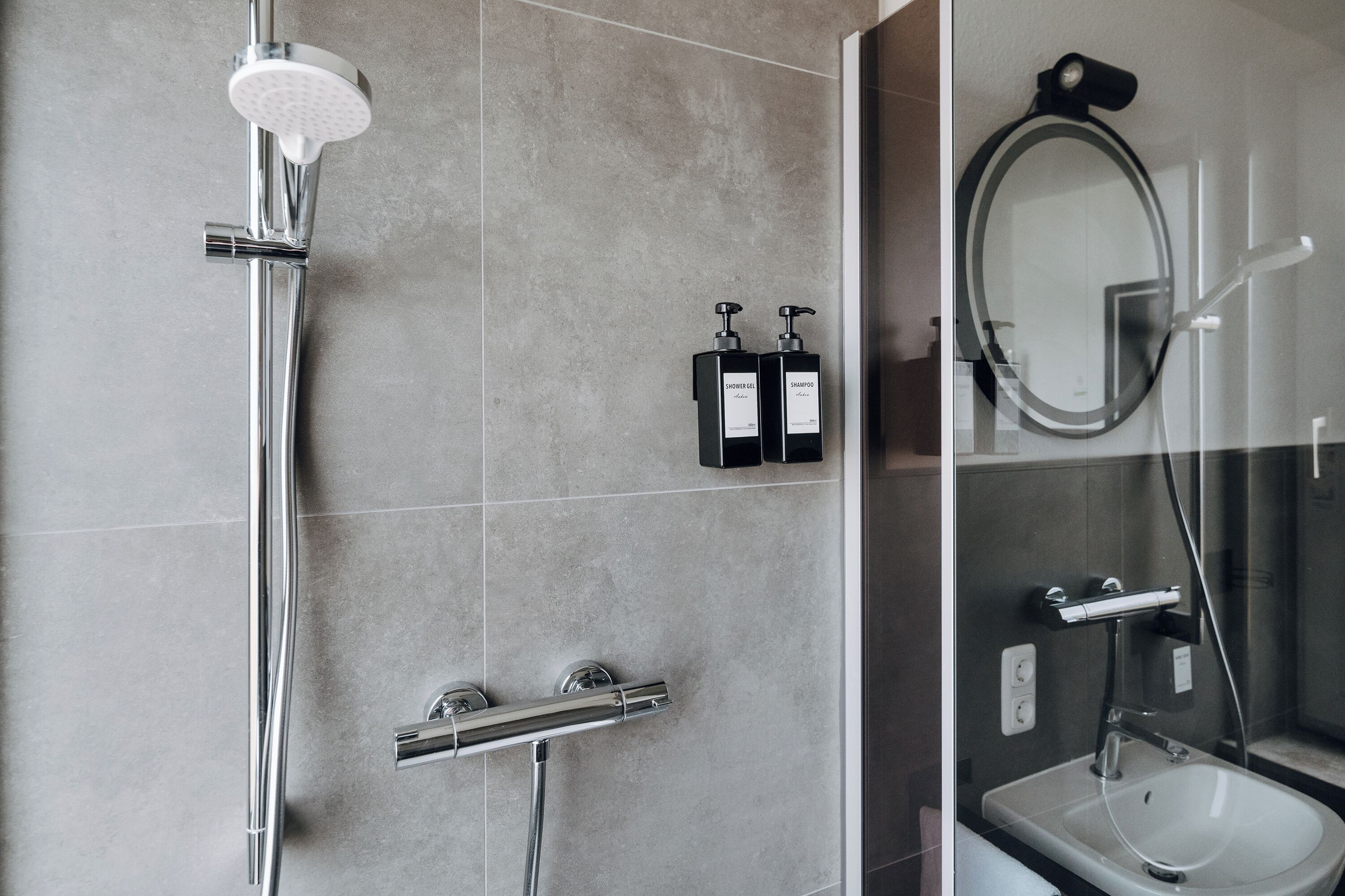 Een moderne badkamer met een douche, wastafel en twee flessen shampoo.