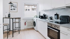 Una cocina moderna con lavadora integrada, horno y ventana con vistas a edificios.