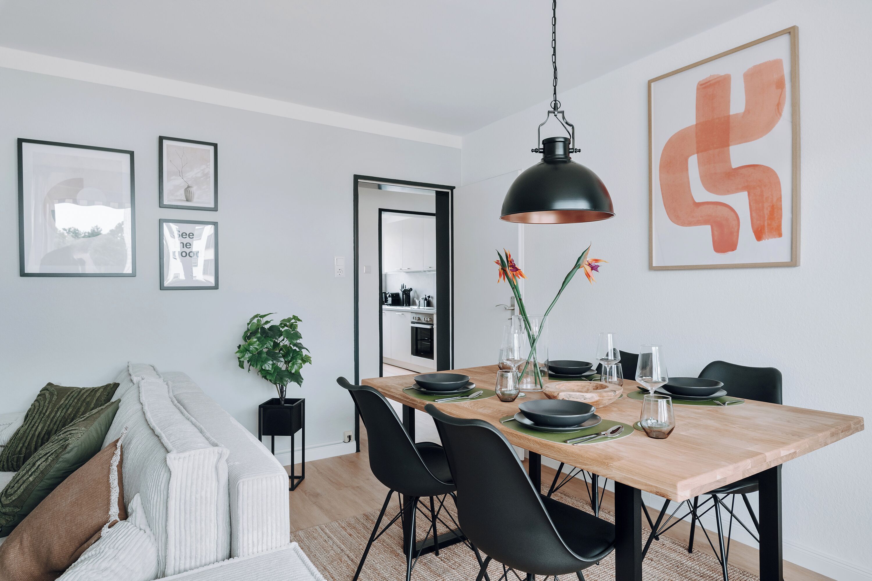 A modern dining area with a wooden table, black chairs, and a hanging pendant light.