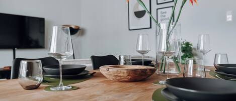 A dining table set with clear glassware, a wooden bowl, and green placemats.