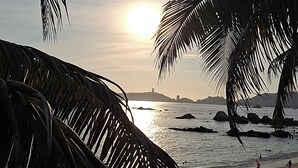 Eine Strandansicht mit Palmen, einem Sonnenuntergang und Blick aufs Meer.