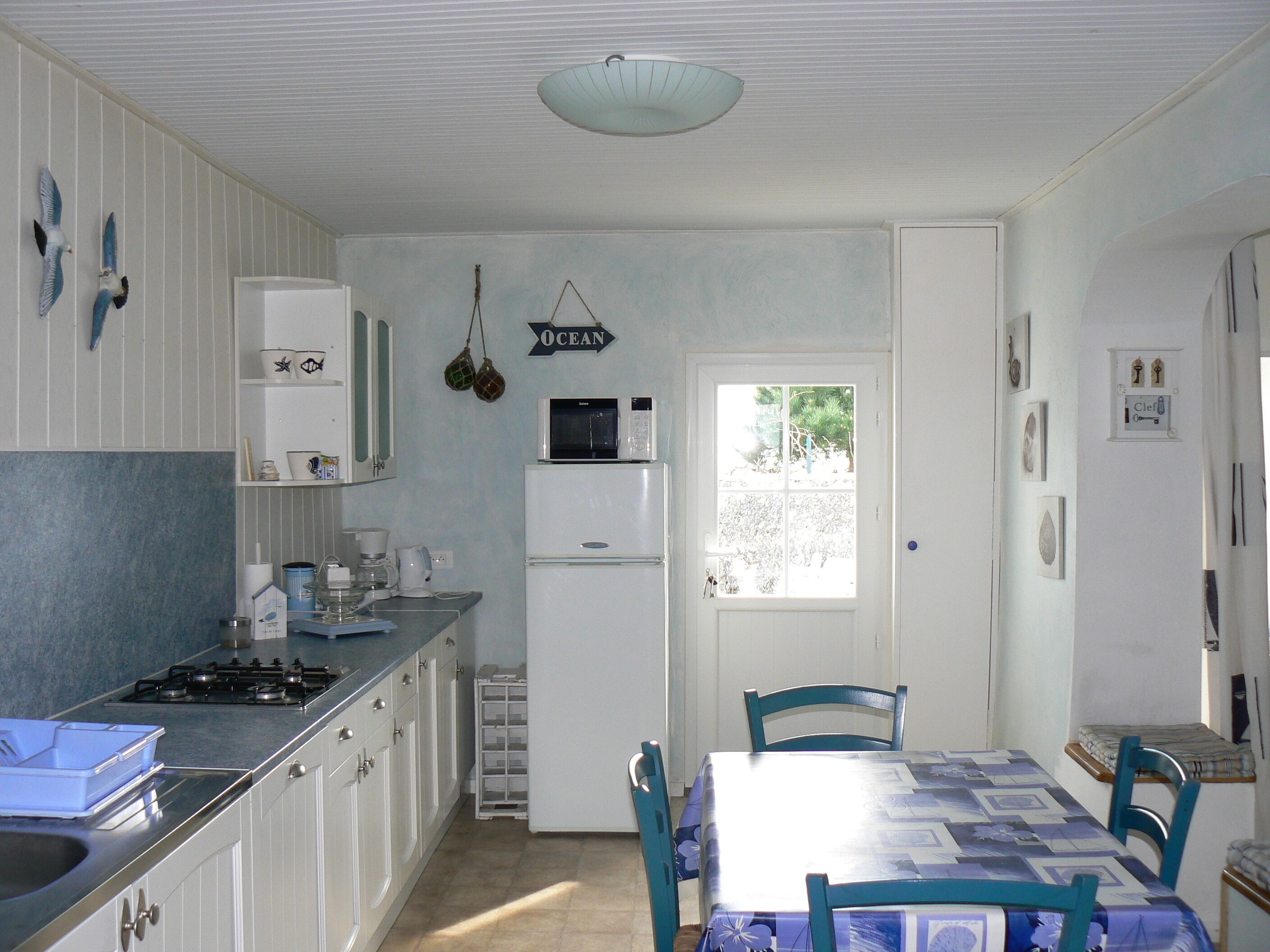 A compact kitchen with white cabinets, a microwave, and a refrigerator. There is a dining table with chairs and a window providing natural light.