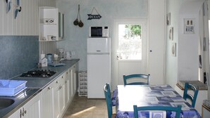 A compact kitchen with white cabinets, a microwave, and a refrigerator. There is a dining table with chairs and a window providing natural light. - Renovated traditional fisherman's cottage 250 m from the beach (L'Épine)