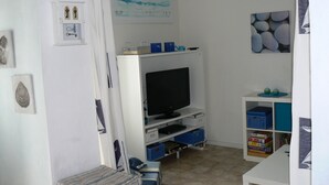 A room with a television on a stand, a small bench, and a shelf with books and decorative items. - Renovated traditional fisherman's cottage 250 m from the beach (L'Épine)