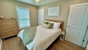 Une chambre à coucher comprenant un lit, une commode, des tables de chevet et une fenêtre avec des stores.