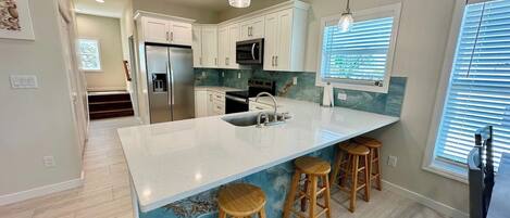 A modern kitchen with white cabinetry, a large island with stools, a built-in microwave, and a refrigerator.