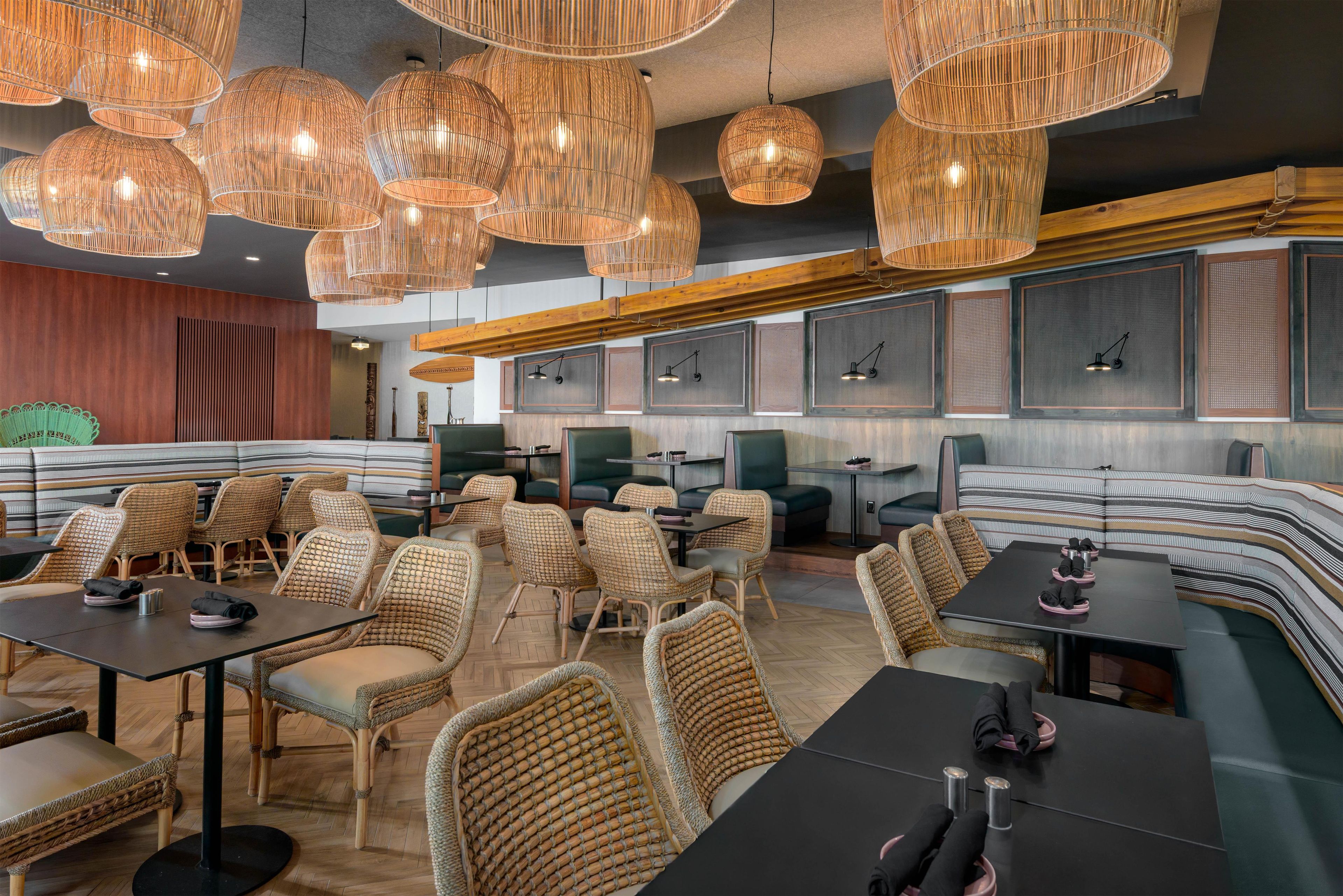 Un intérieur de restaurant moderne avec des meubles en osier, des tables noires et de nombreux lustres en osier suspendus au plafond.