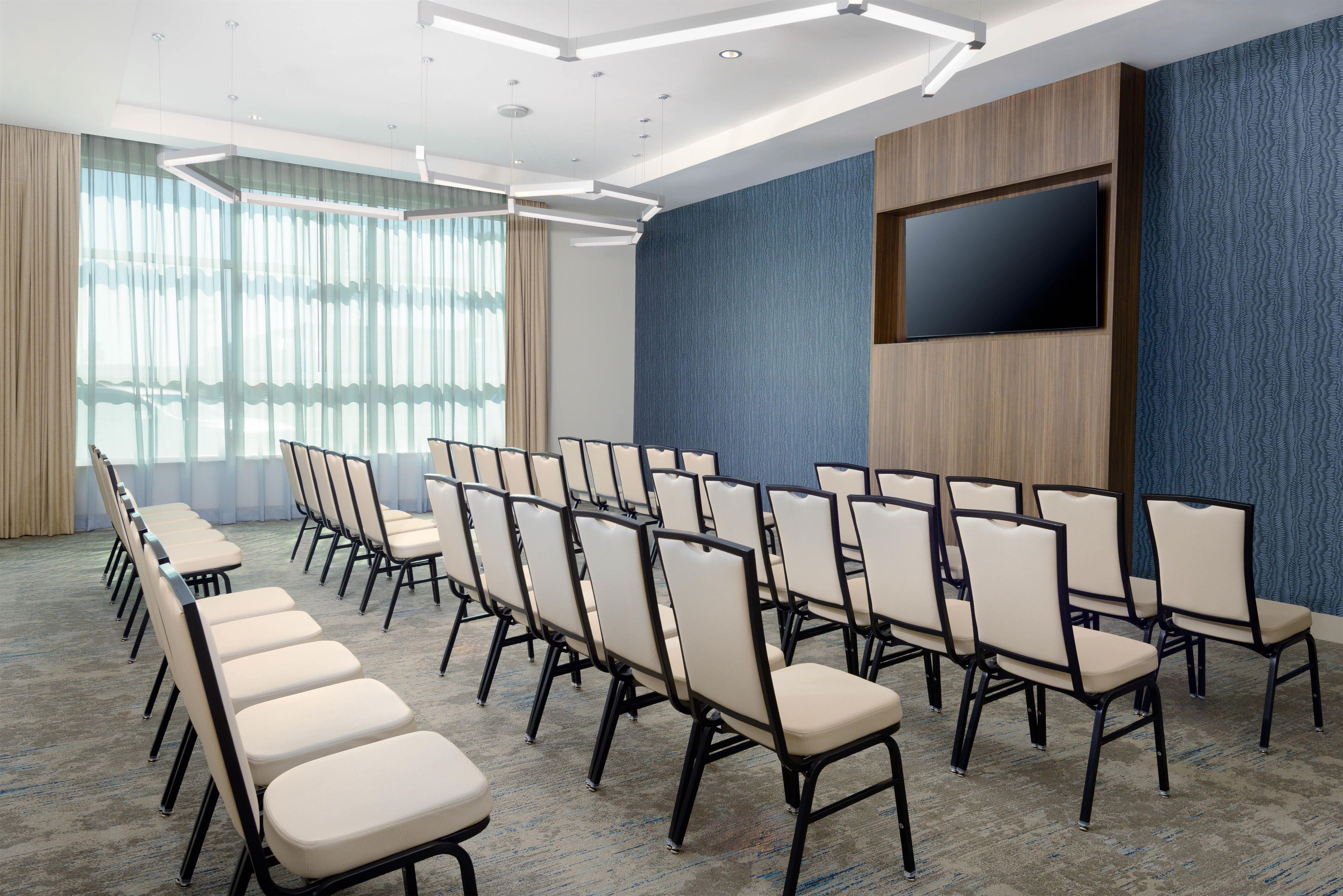 A conference room with rows of chairs, a large flat-screen TV, and a patterned wall.