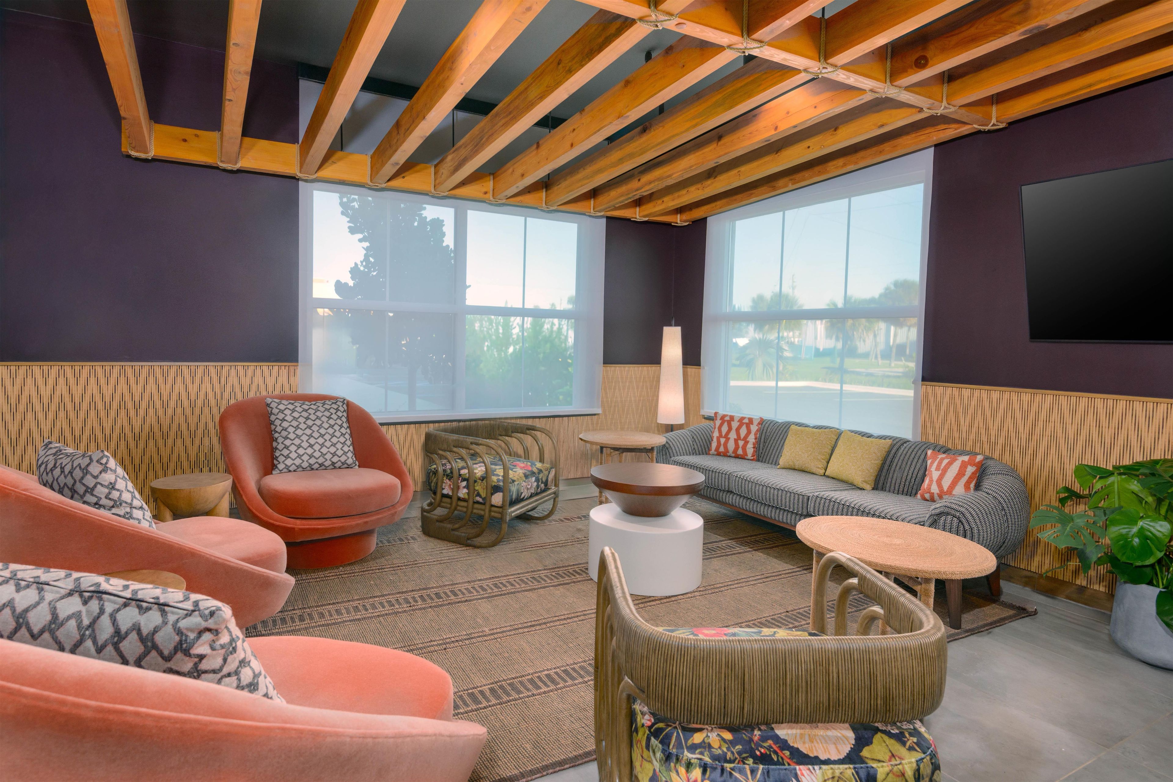 A modern living room with a high ceiling, wooden beams, large windows, and a variety of seating options including a sofa, chairs, and a small table.