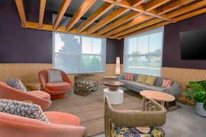 A modern living room with a high ceiling, wooden beams, large windows, and a variety of seating options including a sofa, chairs, and a small table. - Hilton Garden Inn Cape Canaveral near Cocoa Beach (Cape Canaveral)
