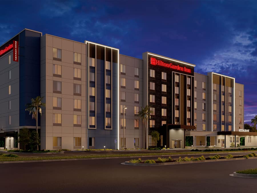 Un hotel moderno con un llamativo letrero de Hilton Garden Inn, varios pisos y una entrada bien iluminada.