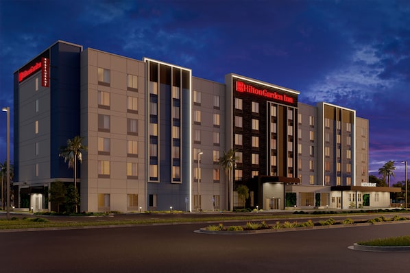 Un hotel moderno con un llamativo letrero de Hilton Garden Inn, varios pisos y una entrada bien iluminada.