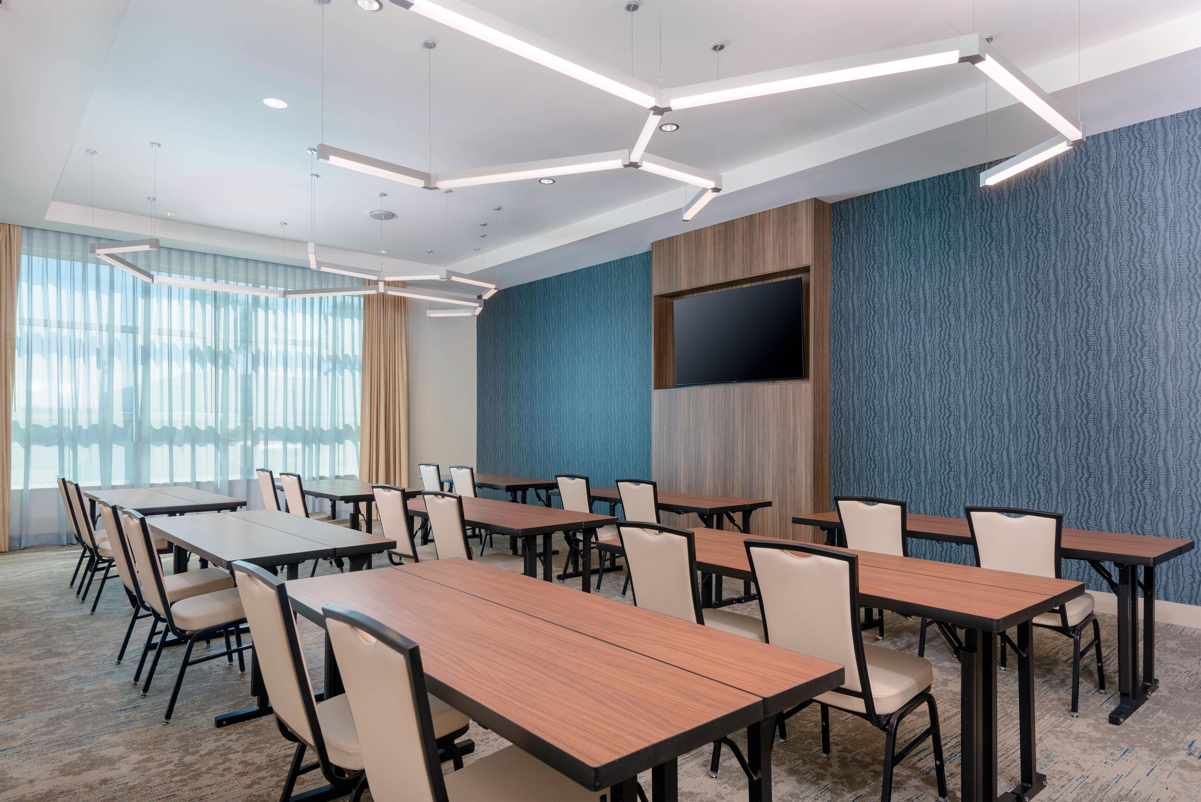 A conference room with multiple tables and chairs, a flat-screen TV mounted on the wall, and a patterned wall.
