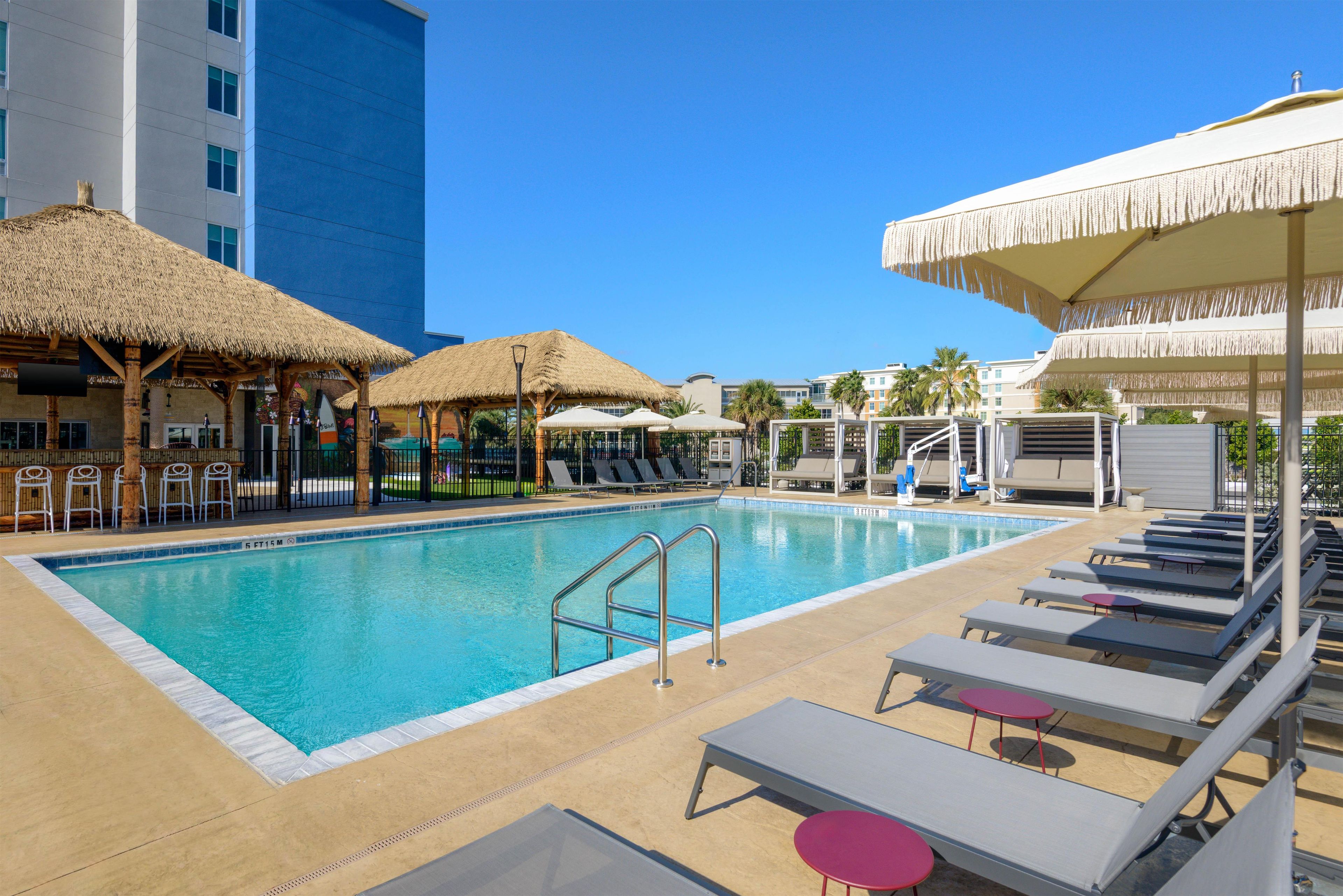 A swimming pool with lounge chairs and umbrellas, surrounded by buildings.