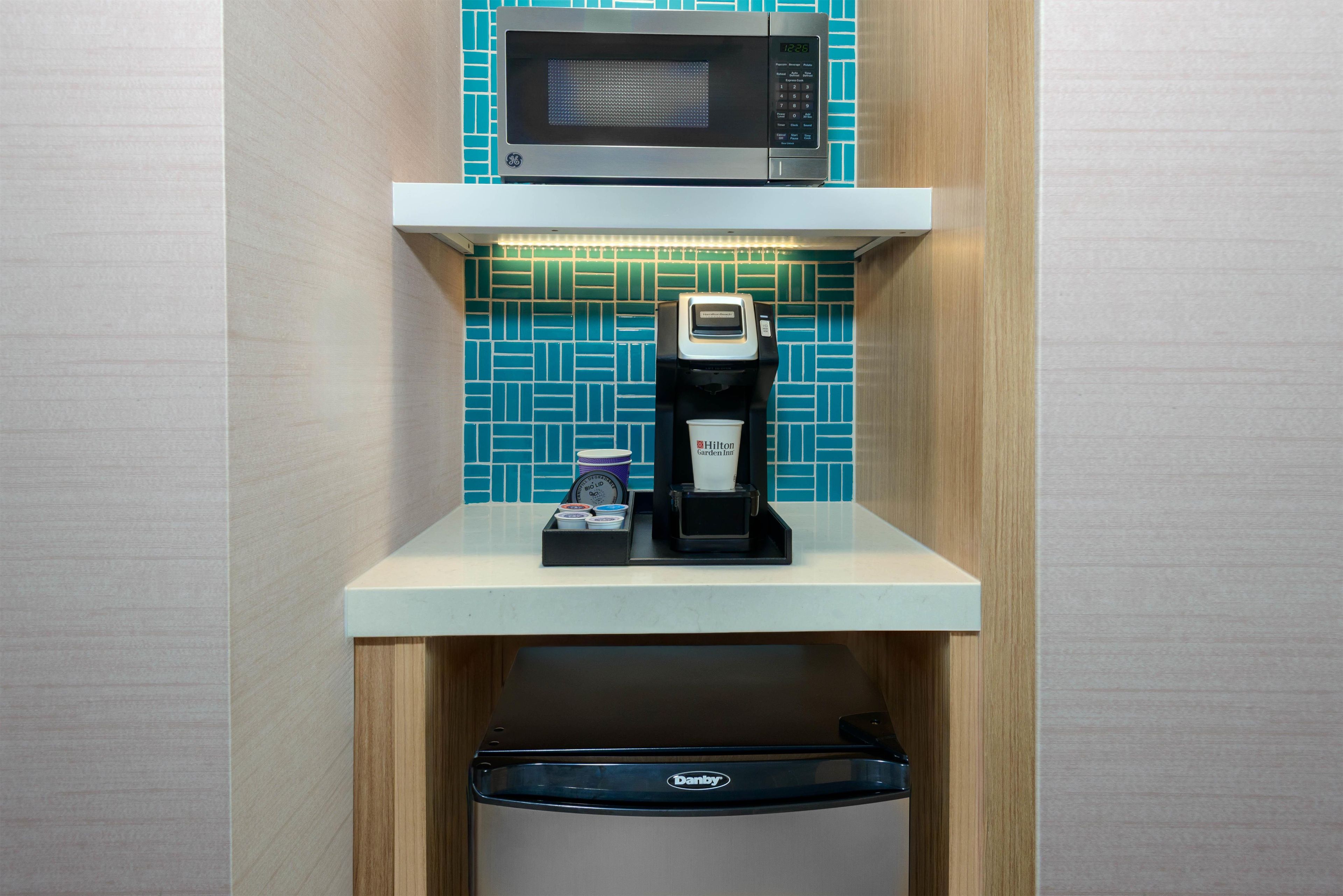 A compact kitchenette with a microwave, coffee machine, and a dishwasher.