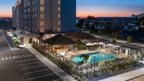 A hotel with a swimming pool, outdoor seating, and a parking lot. - Hilton Garden Inn Cape Canaveral near Cocoa Beach (Cape Canaveral)