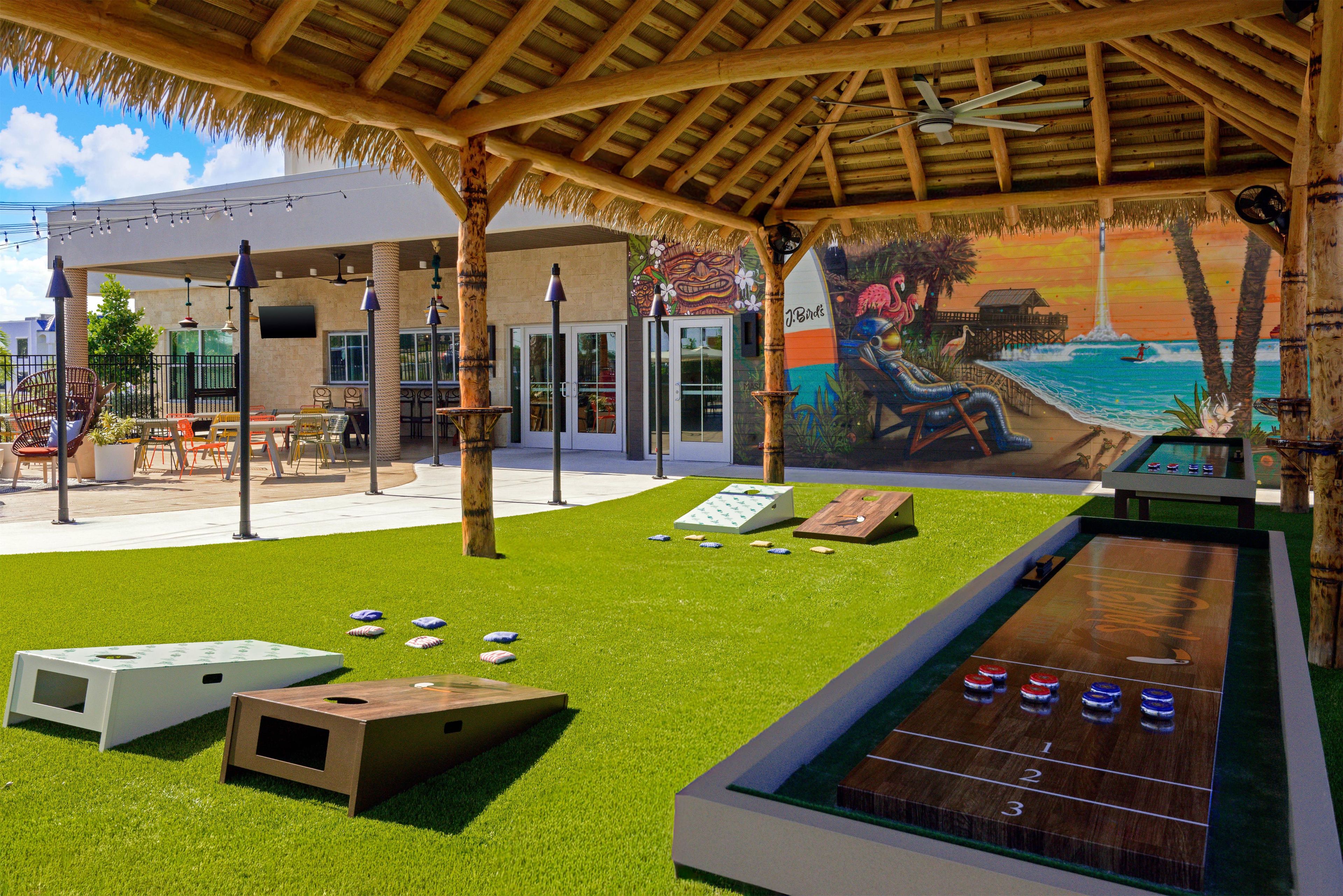 An outdoor area with a pool table, shuffleboard, and a mural of a beach scene.