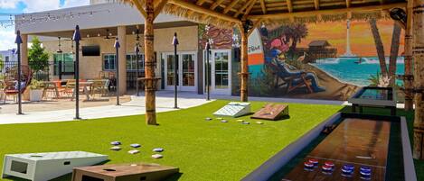 An outdoor area with a pool table, shuffleboard, and a mural of a beach scene.