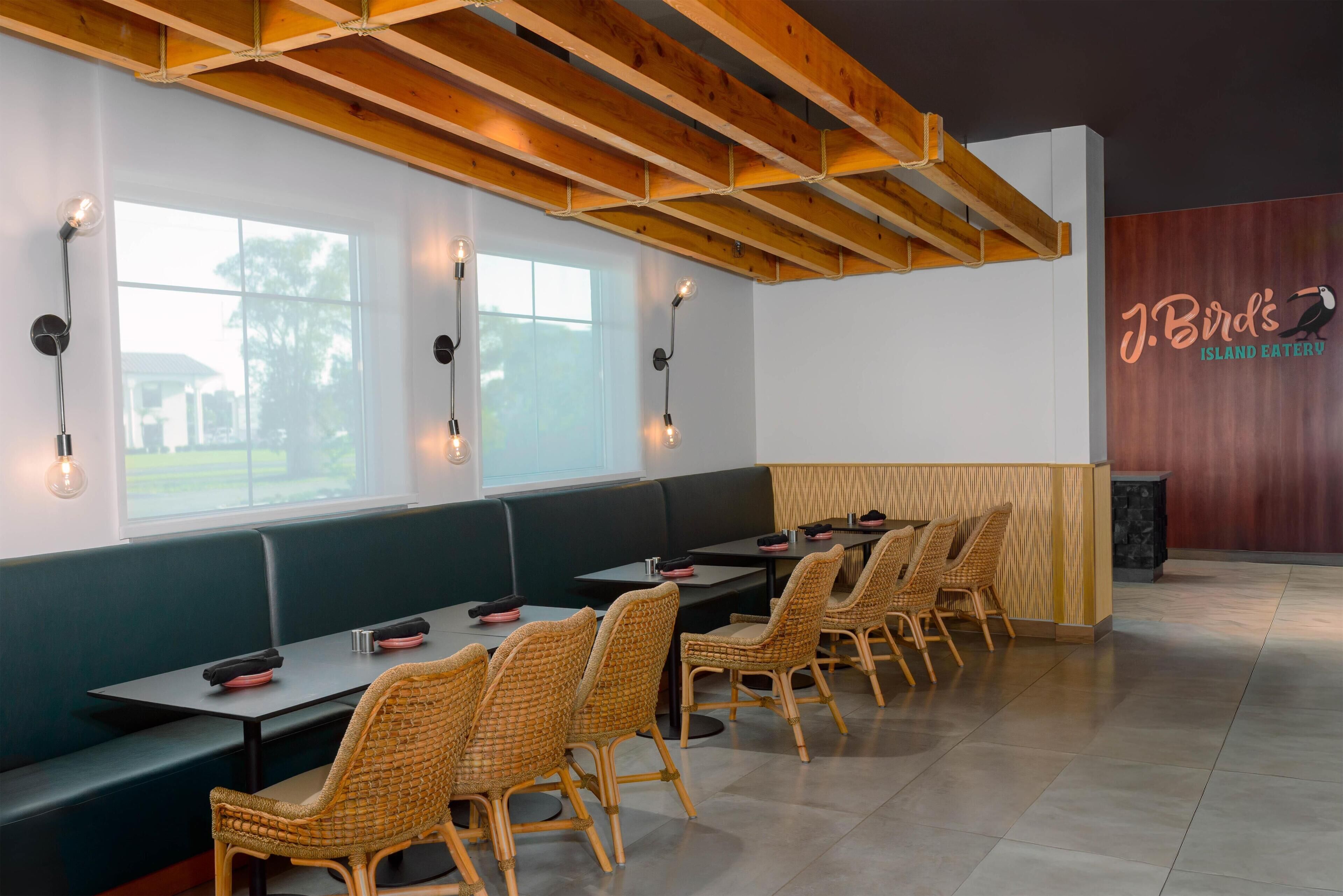 A restaurant interior with wooden beams, green seating, and tables with wicker chairs.