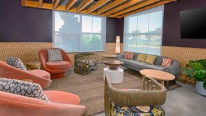 A modern living room with a wooden ceiling, large windows, and a variety of seating options including sofas, chairs, and a round table. - Hilton Garden Inn Cape Canaveral near Cocoa Beach (Cape Canaveral)