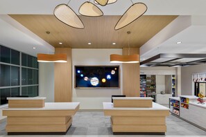 A modern reception area with wooden reception desks, a large wall-mounted TV displaying a space-themed image, and pendant lighting. - Hilton Garden Inn Cape Canaveral near Cocoa Beach (Cape Canaveral)