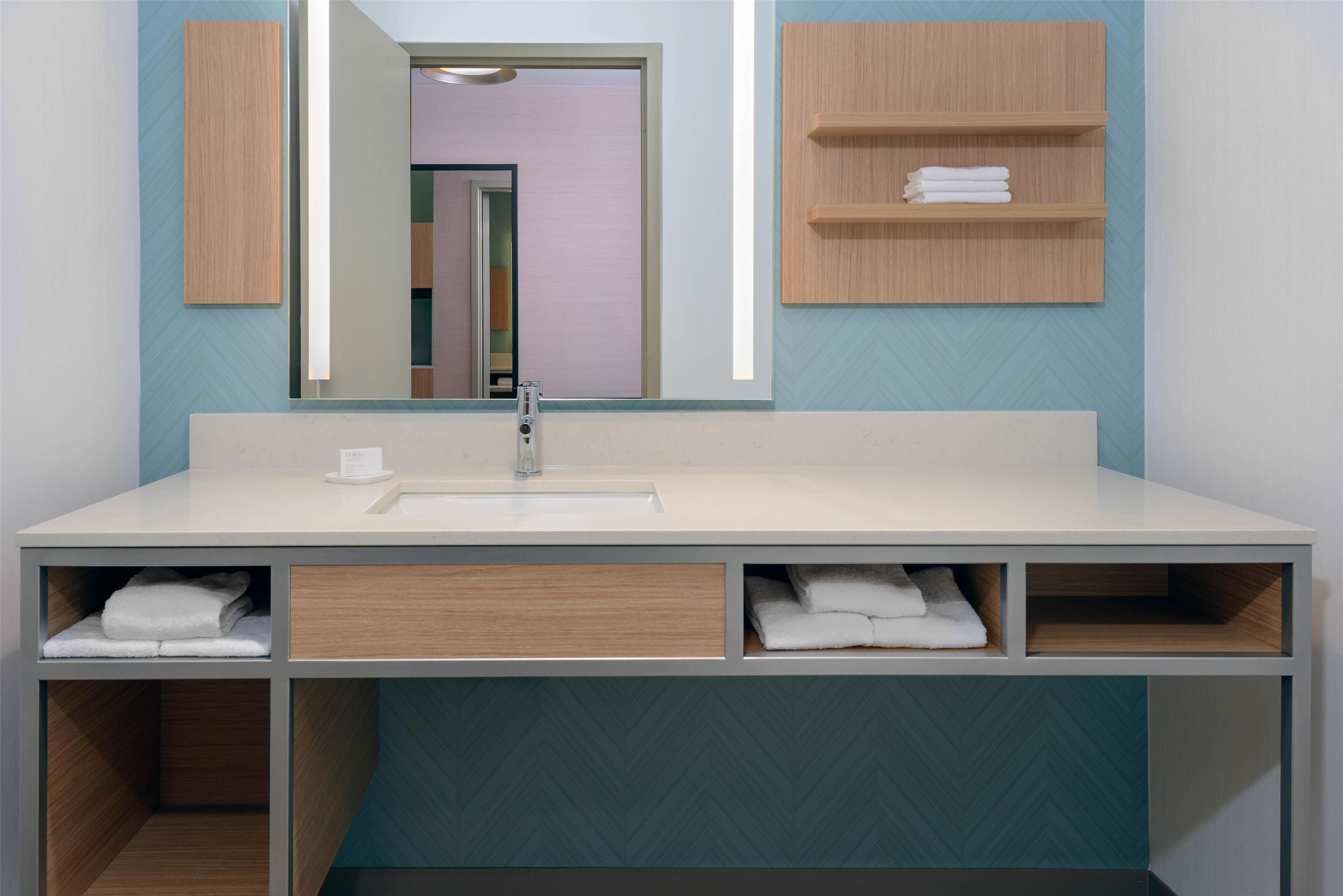 A modern bathroom with a large mirror, a sink, and built-in shelves for towels.