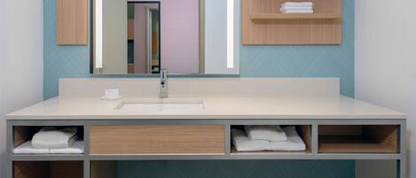 A modern bathroom with a large mirror, a sink, and built-in shelves for towels.