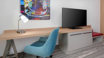 Un espacio de oficina moderno con un escritorio, una silla azul, un televisor y un colorido cuadro abstracto en la pared.
