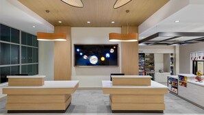 A modern reception area with wooden reception desks, a large wall-mounted TV displaying a space-themed image, and a variety of amenities including a beverage station and a snack bar. - Hilton Garden Inn Cape Canaveral near Cocoa Beach (Cape Canaveral)