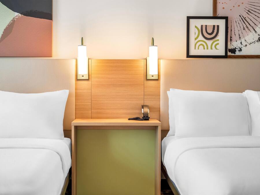 Une chambre d’hôtel avec deux lits, une tête de lit en bois, des lampes de chevet et des œuvres d’art accrochées aux murs.