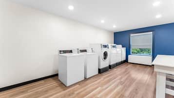 A laundry room with white appliances, a window with a view, and a blue accent wall.