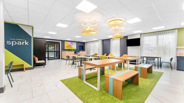 A modern, well-lit meeting room with tables and chairs, a green carpet, and a sign that reads "only takes a spark".